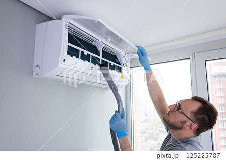 Professional Air Conditioning Maintenance: Man Cleaning and Servicing an AC Unit for Optimal Performance and Efficiency in Modern Indoor Environment Professional Air Conditioning Maintenance: Man Cleaning and Servicing an AC Unit for Optimal Performance and Efficiency in Modern Indoor Environment 125225787