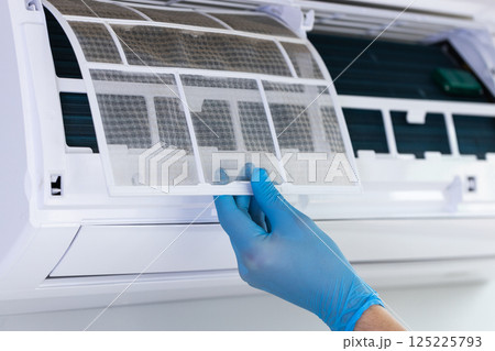 Detailing the Maintenance Process: Carefully Removing a Dusty Air Conditioner Filter with Gloved Hands for Efficient Cleaning and Optimal Performance Enhancement 125225793
