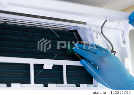 Detailed Examination of an Air Conditioner's Internal Components: A Gloved Hand Performs Maintenance Inside the Machine for Optimal Performance and Efficiency 125225796