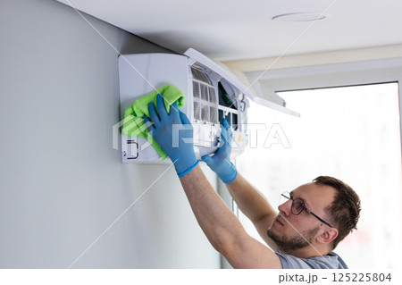 Experienced Technician Carefully Cleaning Air Conditioning Unit with Green Cloth to Ensure Optimal Functionality and Maintain Efficient Performance in Residential Environment 125225804