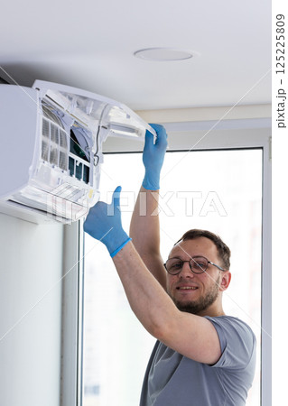 Professional air conditioner technician performing maintenance and cleaning service on an indoor unit, ensuring optimal functionality and comfort in residential spaces. 125225809