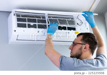 A Skilled Technician Performing Maintenance on an Air Conditioning Unit While Wearing Blue Protective Gloves and Carefully Inspecting the Filters Inside the System A Skilled Technician Performing Maintenance on an Air Conditioning Unit While Wearing Blue Protective Gloves and Carefully Inspecting the Filters Inside the System 125225936