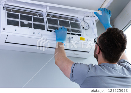 Individual Performing Routine Maintenance on Air Conditioning Unit While Wearing Blue Gloves, Ensuring Clean and Efficient Operation for Comfortable Indoor Environment 125225938