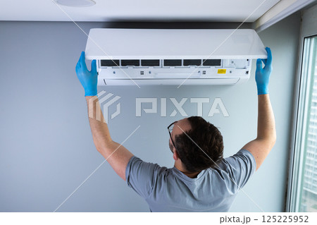 Technician Performing Maintenance on an Air Conditioning Unit While Wearing Protective Gloves in a Modern Indoor Setting Technician Performing Maintenance on an Air Conditioning Unit While Wearing Protective Gloves in a Modern Indoor Setting 125225952