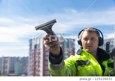 Professional Window Cleaner at Work on a High-Rise Building, Ensuring Clear Views While Embracing Urban Life and Safety in a Bright, Blue Sky Atmosphere Professional Window Cleaner at Work on a High-Rise Building, Ensuring Clear Views While Embracing Urban Life and Safety in a Bright, Blue Sky Atmosphere 125226031