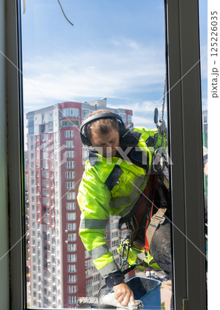 Skilled Window Cleaner Bravely Working on High Rise Building, Ensuring Crystal Clear Windows and Safety with Protective Gear and Harness from Extreme Heights Employing Professional Techniques Skilled Window Cleaner Bravely Working on High Rise Building, Ensuring Crystal Clear Windows and Safety with Protective Gear and Harness from Extreme Heights Employing Professional Techniques 125226035