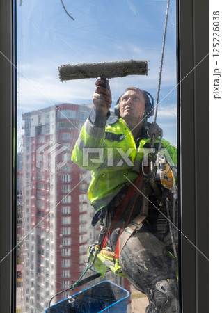 Professional Window Cleaner Working at Heights with Safety Gear and Equipment, Showing Expertise in High-Rise Cleaning While Ensuring Safety and Quality Standards on a Sunny Day Professional Window Cleaner Working at Heights with Safety Gear and Equipment, Showing Expertise in High-Rise Cleaning While Ensuring Safety and Quality Standards on a Sunny Day 125226038