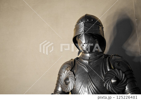 Front view of medieval shiny armor with details and white wall in background. Front view of medieval shiny armor with details and white wall in background. 125226481