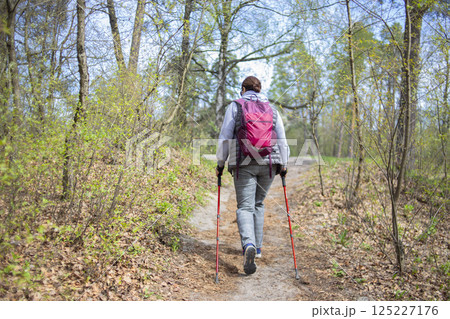 A pensioner woman practicing Nordic walking in the forest A pensioner woman practicing Nordic walking in the forest 125227176