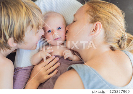 Mother and older son admiring their newborn baby in a cozy infant nest. Family bonding and sibling love concept 125227969