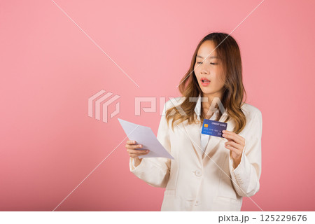 Portrait of Asian young woman holding paper calculating bills on hand and credit card for payment, female person problem she hold worried over bill, studio shot isolated on pink background Portrait of Asian young woman holding paper calculating bills on hand and credit card for payment, female person problem she hold worried over bill, studio shot isolated on pink background 125229676