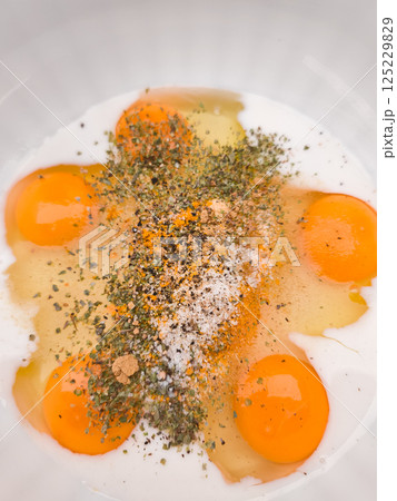 Raw eggs with spices and milk ready for whisking in a bowl Raw eggs with spices and milk ready for whisking in a bowl 125229829