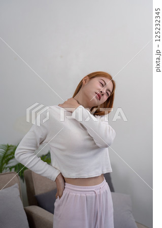 Young woman stretching neck and holding her shoulder, seeking relief from discomfort in home environment 125232345