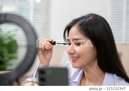 Beauty broker applying mascara during a live broadcast showcasing cosmetics and makeup tips 125232347