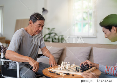 Father and son engaged in a chess game in a bright living room, highlighting family bonding and strategic interaction. Father and son engaged in a chess game in a bright living room, highlighting family bonding and strategic interaction. 125232381