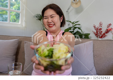 Overweight woman offering a fresh salad, promoting healthy weight loss. 125232422
