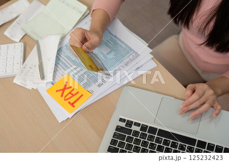 Woman managing taxes with a credit card and financial documents on a desk. 125232423