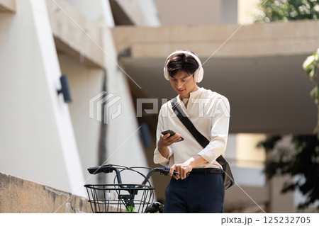 Modern Commuting and Digital Connectivity. A young man checks his phone while parked on his bicycle, enjoying a moment of tech-savvy relaxation. 125232705