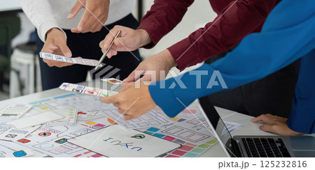 Collaboration and UX Design. Team members engaged in a collaborative UX design meeting, analyzing prototypes and sketching ideas together. 125232816