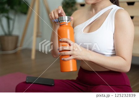 Hydration and Wellness. A woman prepares to hydrate with an orange water bottle after a workout session. 125232839