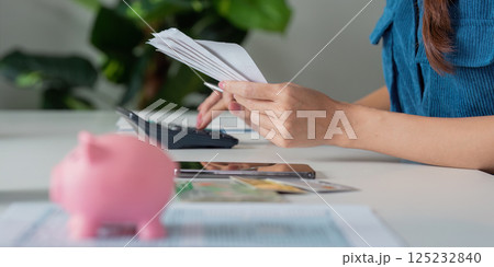 Savings and Budgeting Techniques. A person organizing bills while a piggy bank sits prominently on the table. 125232840
