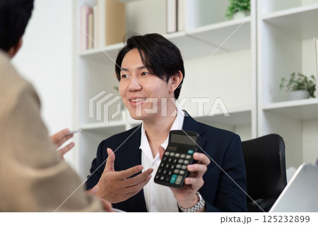 Professional Guidance in Real Estate Transactions. A smiling agent explaining investment options using a calculator. 125232899