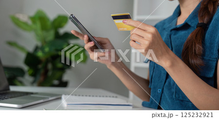 Financial Management and Saving. A young woman engaging in online banking, using her smartphone and credit card to manage her finances. Financial Management and Saving. A young woman engaging in online banking, using her smartphone and credit card to manage her finances. 125232921