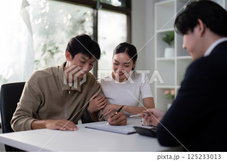 Finalization and Joy. A couple happily fills out paperwork with their agent during a real estate purchase. Finalization and Joy. A couple happily fills out paperwork with their agent during a real estate purchase. 125233013
