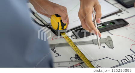 Measuring and Planning. A colleague measuring dimensions of a building plan with precision tools. 125233093