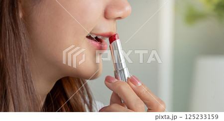 Lipstick and Glamour. A woman applying vibrant red lipstick as a finishing touch to her makeup. 125233159