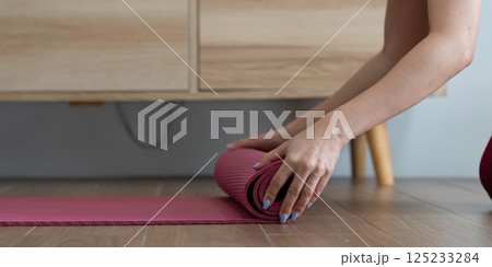 Yoga and Relaxation. A woman rolling up her yoga mat after a refreshing session. Yoga and Relaxation. A woman rolling up her yoga mat after a refreshing session. 125233284