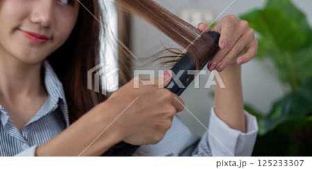 Hair Styling and Beauty Routine. A woman using a flat iron to create sleek hair. Hair Styling and Beauty Routine. A woman using a flat iron to create sleek hair. 125233307