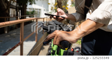 Sustainability and Sharing Economy. A person prepares to ride an electric scooter while using his smartphone. Sustainability and Sharing Economy. A person prepares to ride an electric scooter while using his smartphone. 125233349