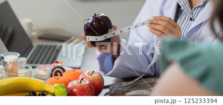 Nutritionist Consultation and Healthy Choices. A nutritionist measures an apple while discussing healthy eating habits with a client. Nutritionist Consultation and Healthy Choices. A nutritionist measures an apple while discussing healthy eating habits with a client. 125233394