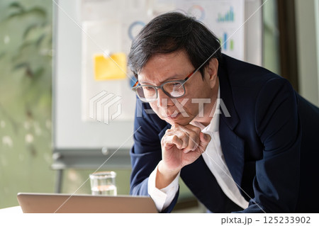 Elderly professional analyzing financial reports and data on a laptop. 125233902