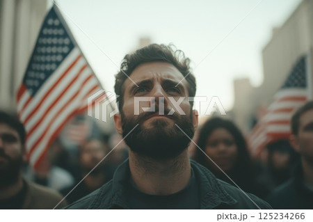 A man with a beard stands in front of a crowd holding an American flag A man with a beard stands in front of a crowd holding an American flag 125234266