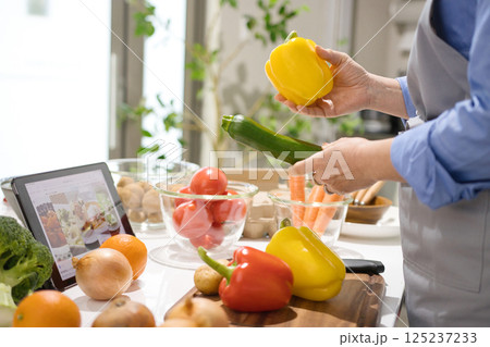 タブレットを見ながら料理をするミドル女性 125237233