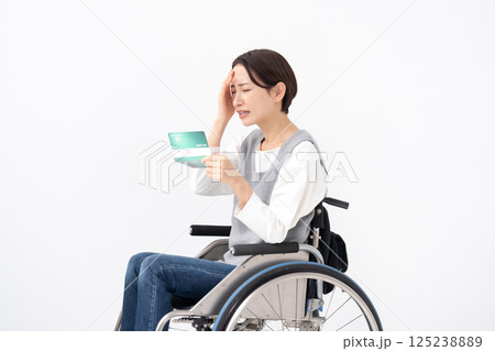 通帳を見て落ち込む車椅子の女性 125238889