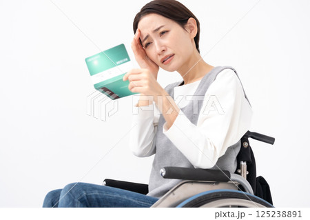 通帳を見て落ち込む車椅子の女性 125238891