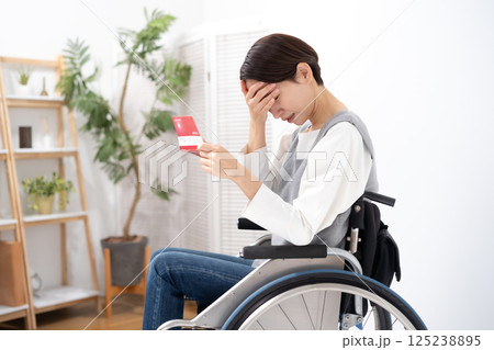 通帳を見て落ち込む車椅子の女性 125238895