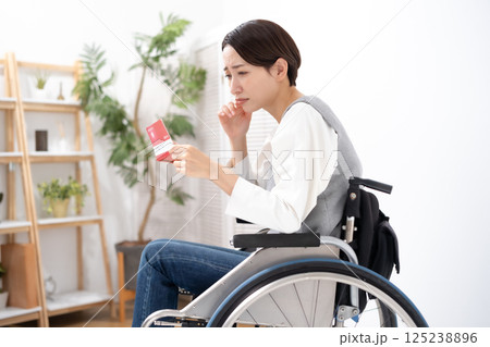通帳を見て落ち込む車椅子の女性 125238896