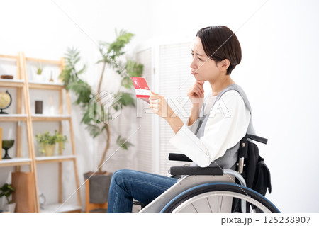 通帳を見て落ち込む車椅子の女性 125238907