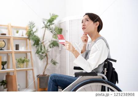 通帳を見て落ち込む車椅子の女性 125238908