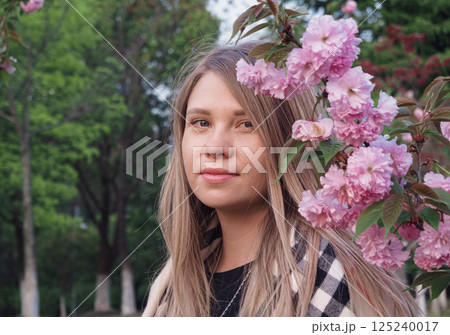 Young woman posing among blooming pink flowers in a botanical garden during springtime 125240017