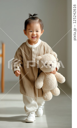 cheerful baby girl learning to walk while holding teddy bear in bright indoor space 125242616