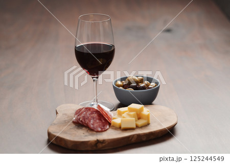 olives, salami and vintage cheese with glass of red wine on walnut table olives, salami and vintage cheese with glass of red wine on walnut table 125244549