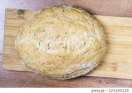 Top view of round loaf of homemade rye bread placed on a wooden bamboo cutting board on a hardwood texture countertop. Baking concept, symbol of happy family life 125245229