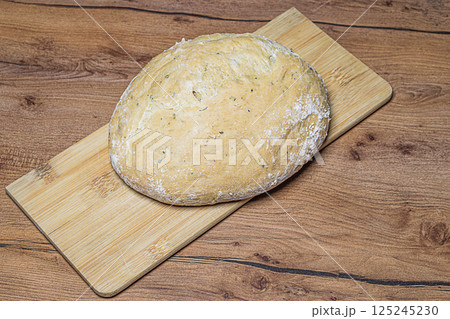 First-person view of round loaf of homemade rye bread placed on a wooden bamboo cutting board on a hardwood texture countertop. Baking concept, symbol of happy family life 125245230