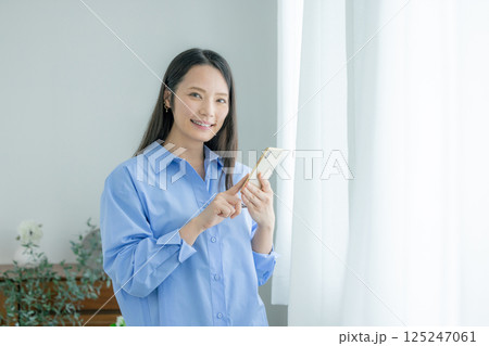 窓際でスマホを操作するミドル女性 125247061