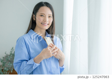 窓際でスマホを操作するミドル女性 125247063
